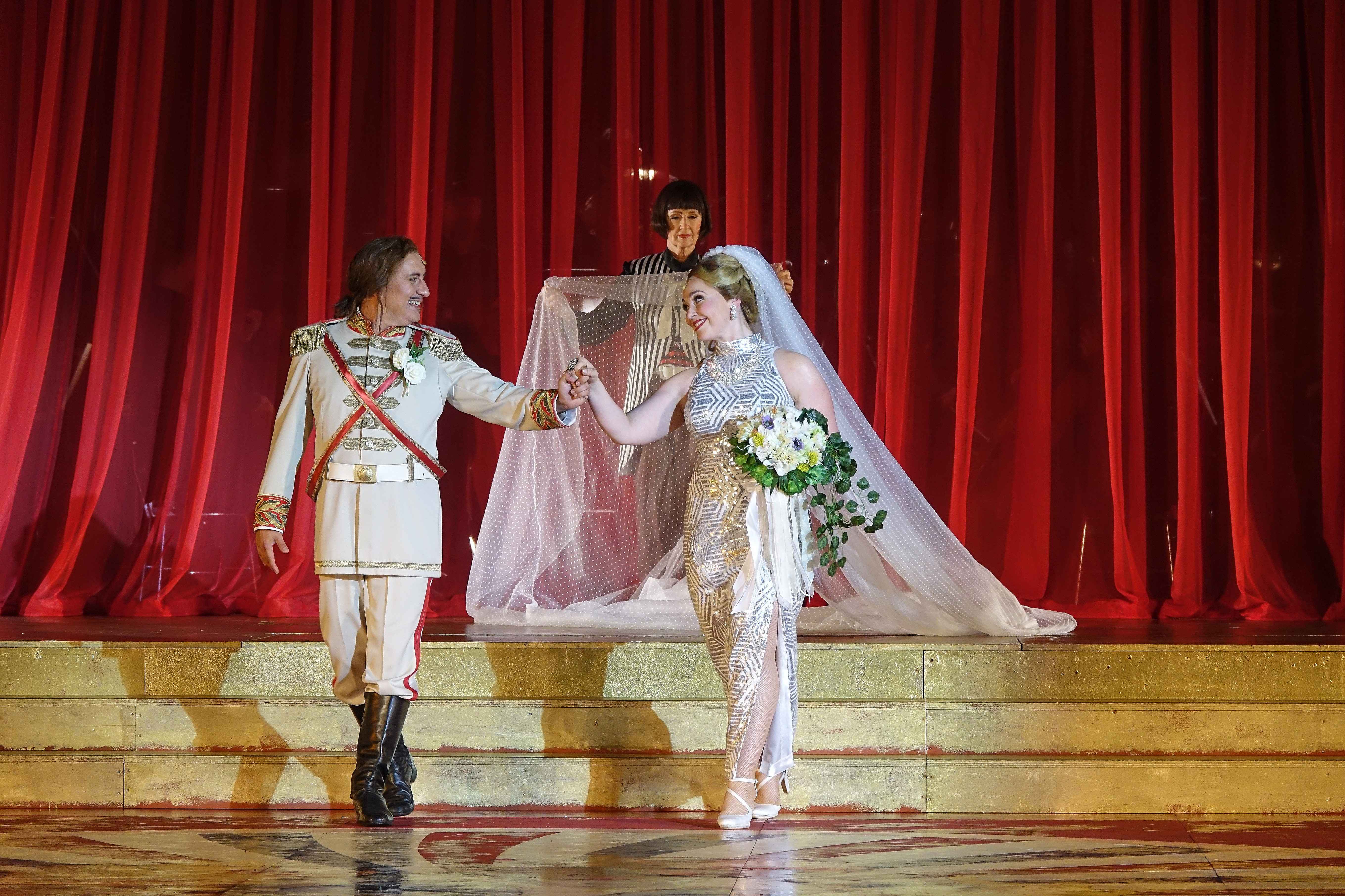 Ein uniformierter Herr geht Hand in Hand mit einer Dame im Glitzerkleid und Schleier