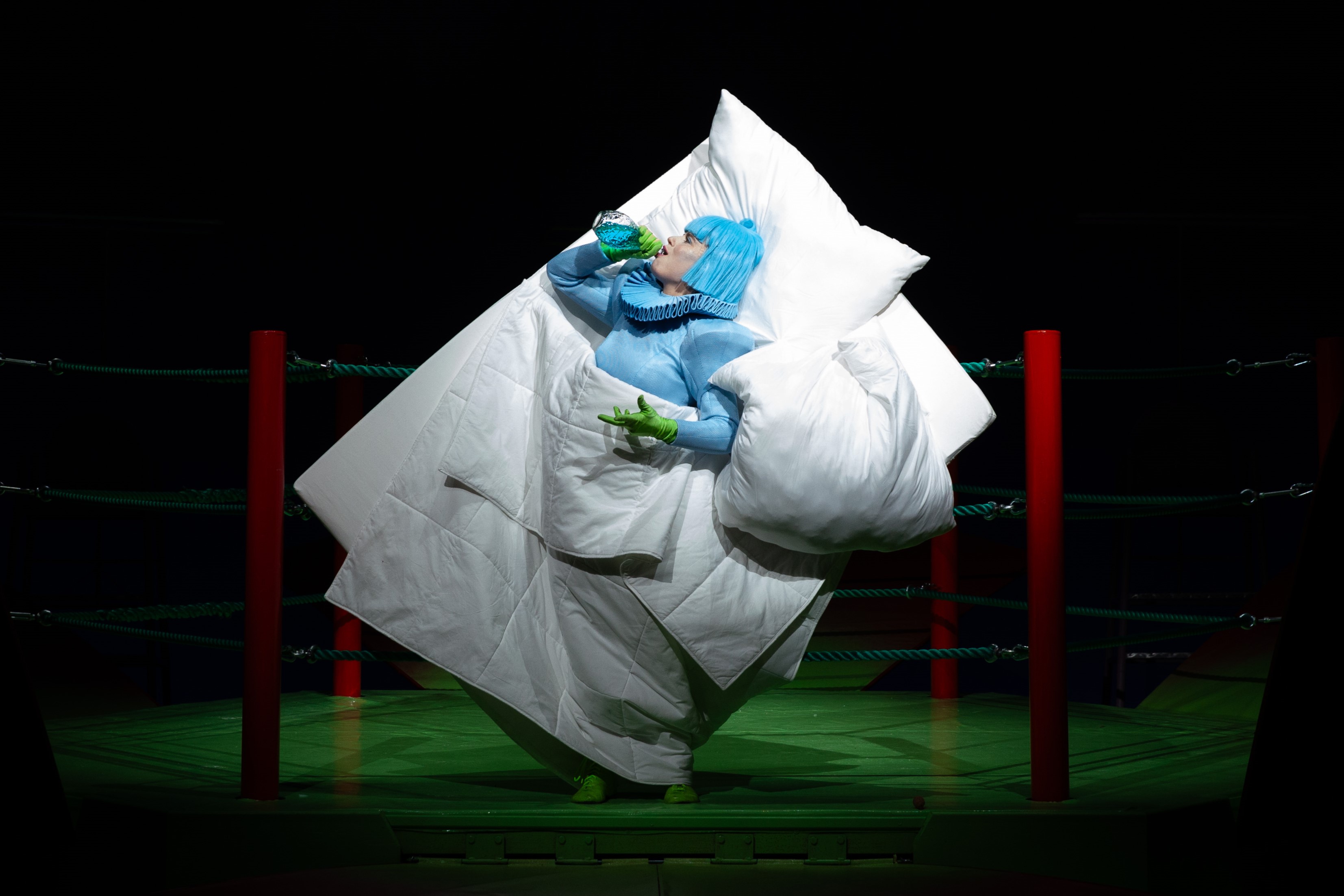 Julia trinkt eine blaue Flüssigkeit in einem angedeuteten Bett