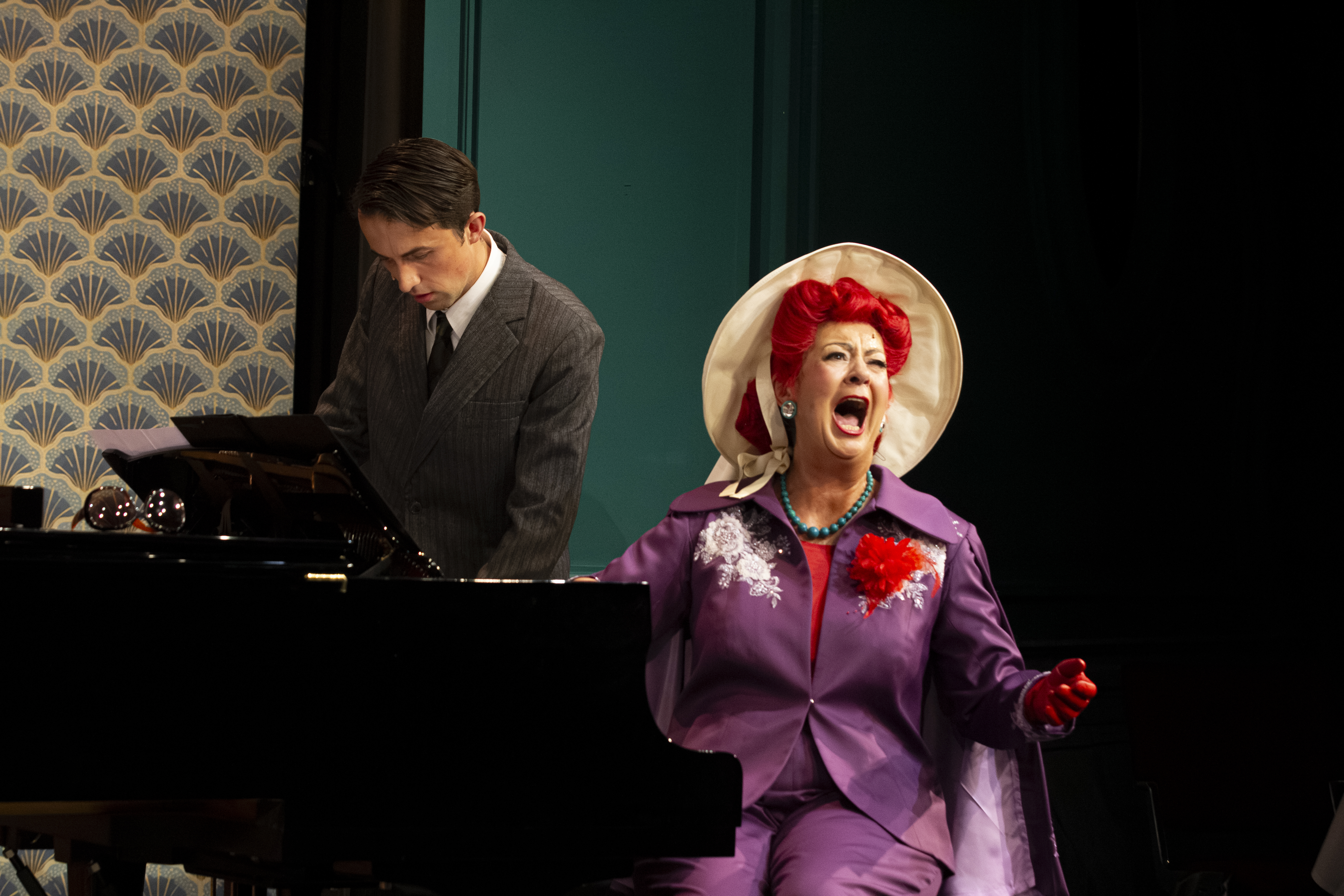 Ein mann am Piano, eine Frau im lila Kostüm und Hut, singt