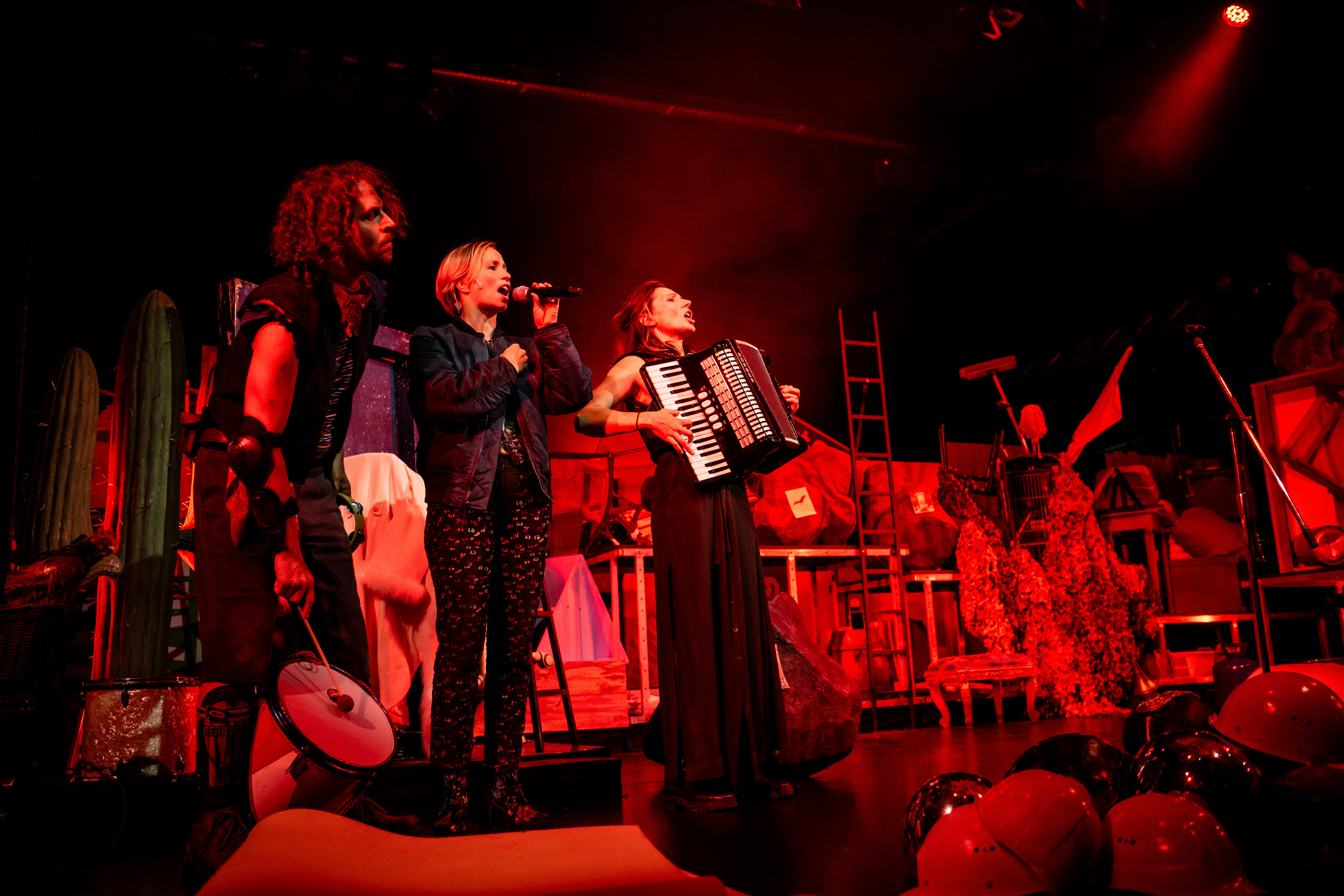 Ein Mann und zwei Frauen beim Musizieren auf einer rot ausgeleuchteten Bühne