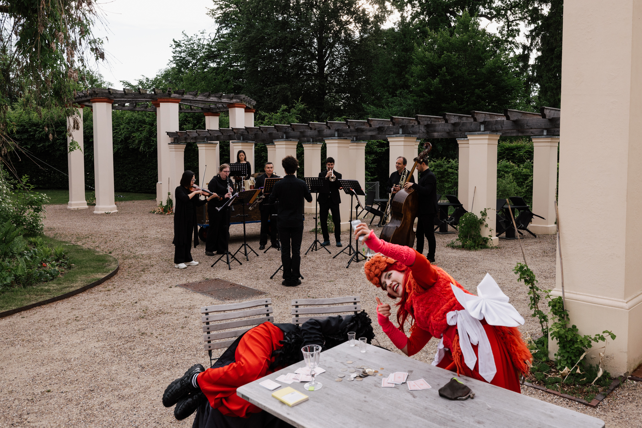 Marketenderin und Teufel an einem Tisch, im Hintergrund spielt ein kleines Orchester